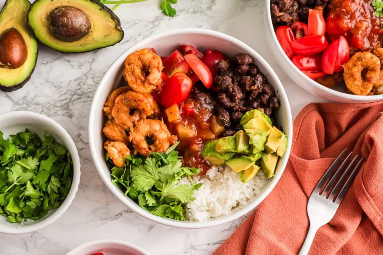 Blackened shrimp and rice in a bowl with avocado and orange napkin on the sides.