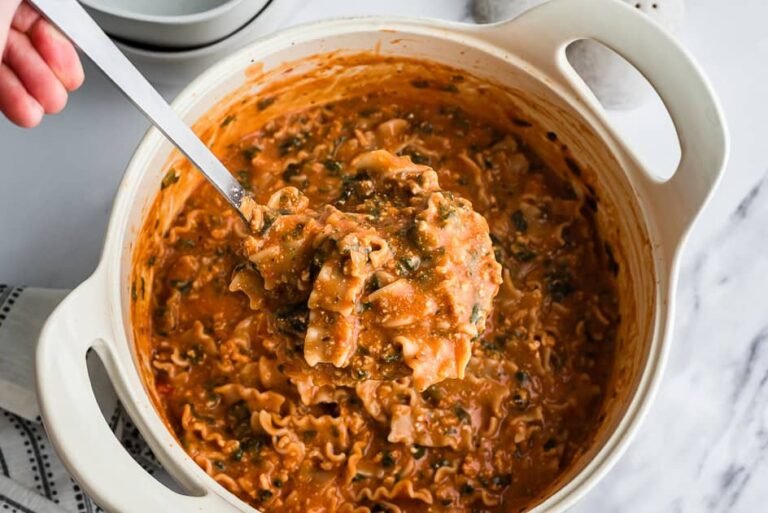 Large spoonful of ground chicken lasagna soup being scooped from pot.