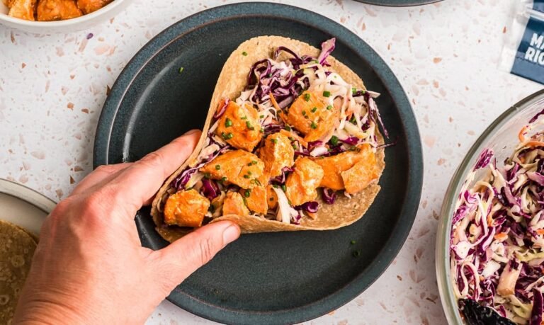 Hand holding a buffalo salmon taco on a blue plate.